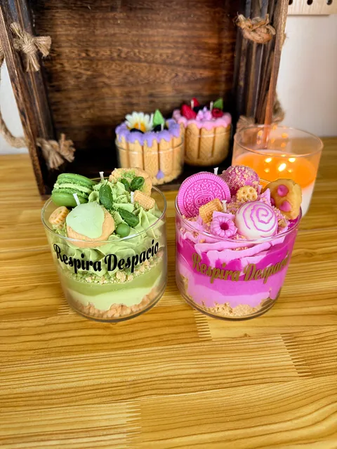 Velas en vasos con capas verdes y rosas y decoraciones de colores sobre una mesa de madera