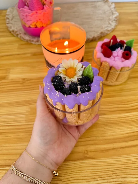 Vela con forma de pastel, cubierta lila, flores y decoraciones de frutos oscuros