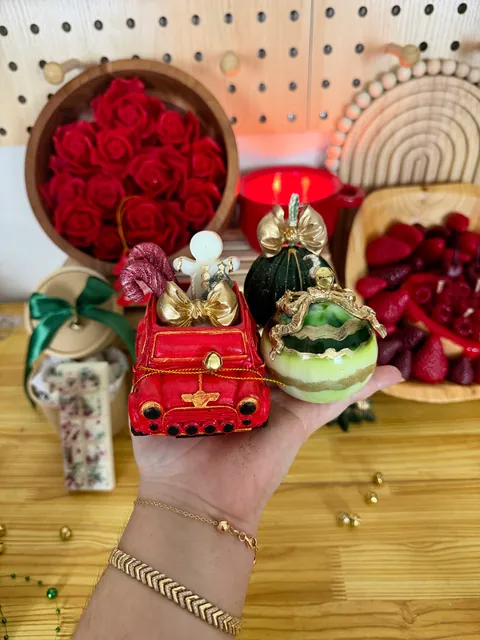 Piezas decorativas navideñas sostenidas en una mano, con un vehículo rojo y formas blancas y verdes.